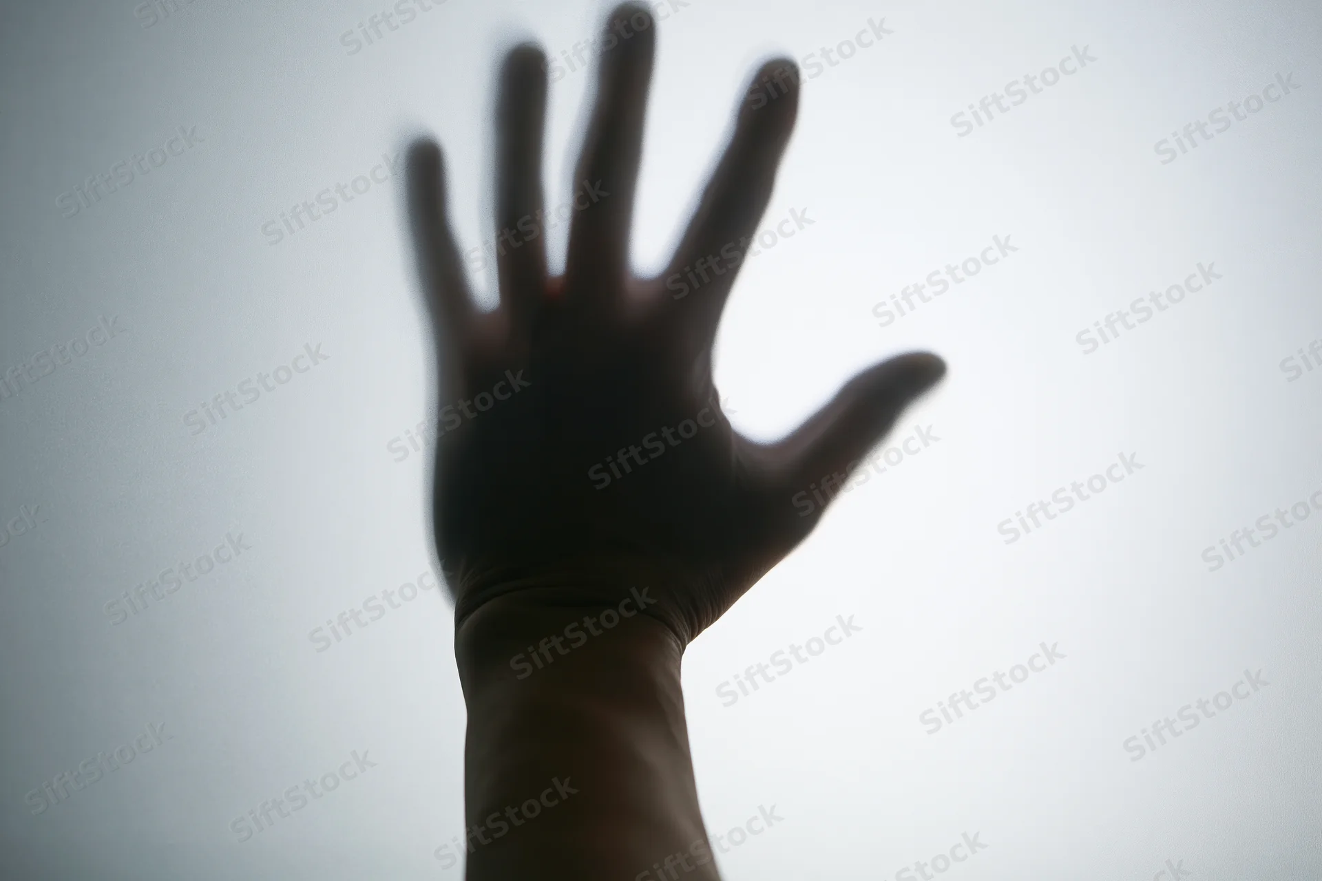 Silhouette of a hand pressed against frosted glass in a dim interior