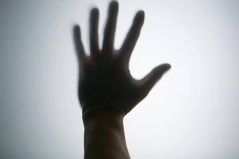 Silhouette of a hand pressed against frosted glass in a dim interior
