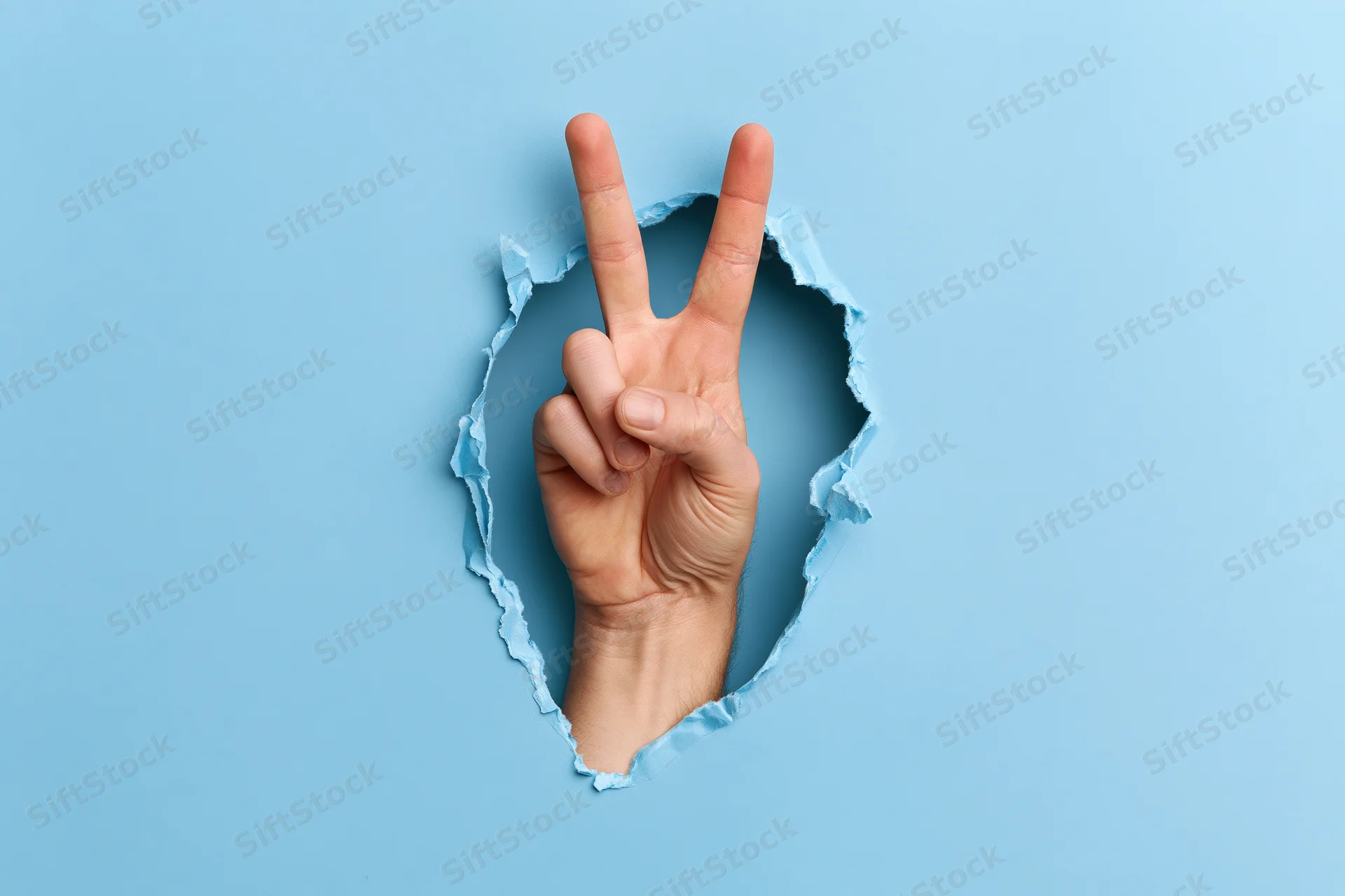 Hand making peace sign through torn blue paper background