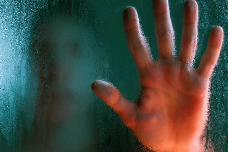 Hand pressed against fogged glass in a steamy bathroom