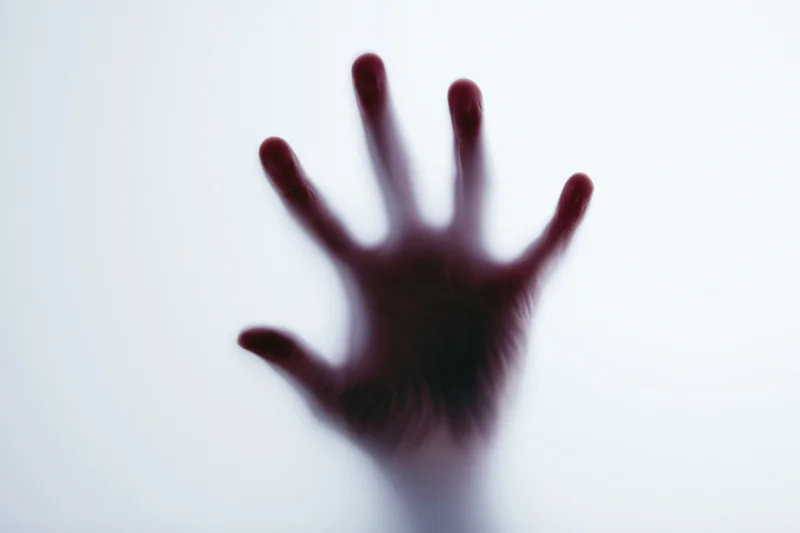 Hand pressed against frosted glass in a blurred silhouette