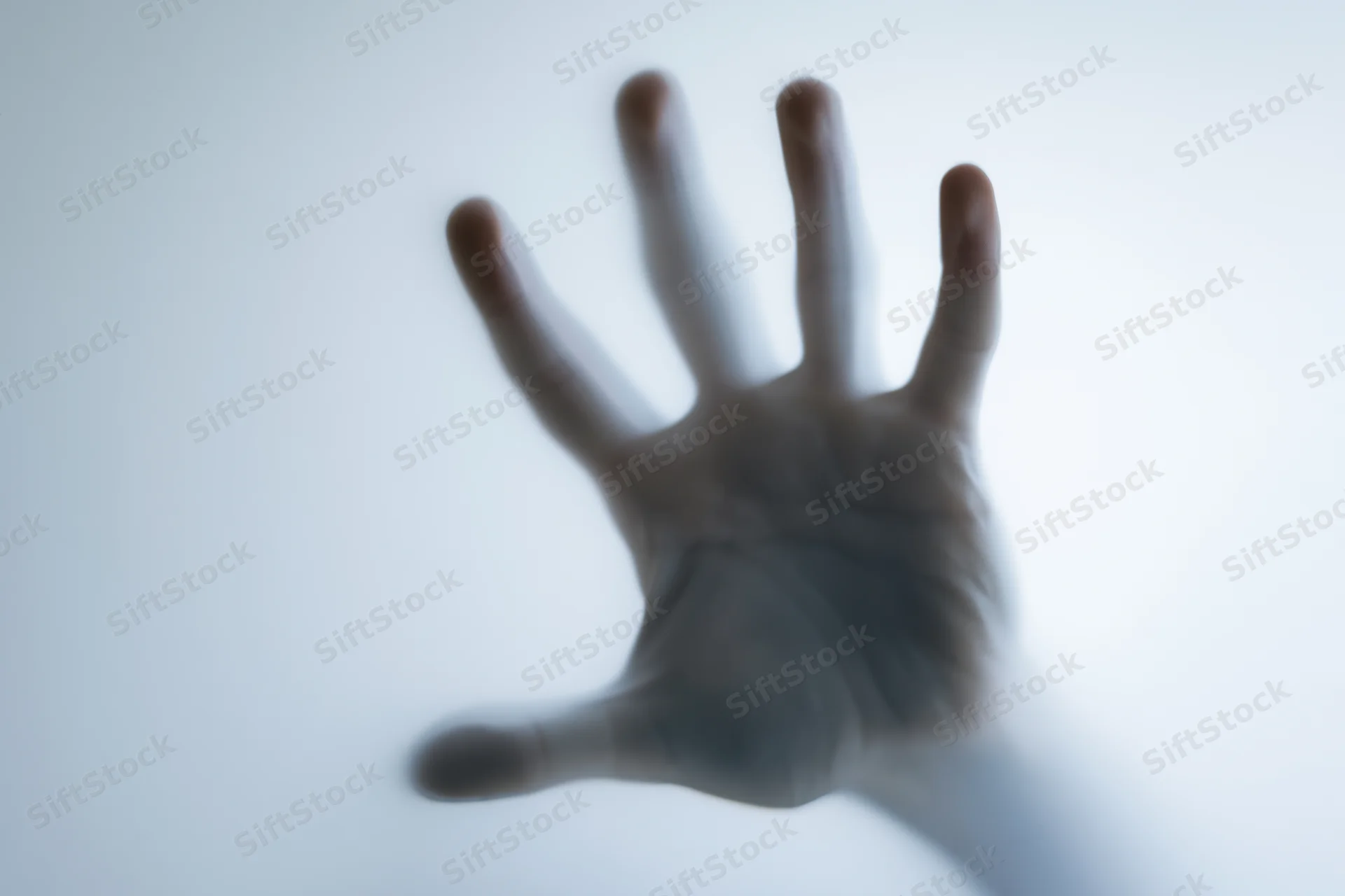 Hand pressing against frosted translucent glass with blurred details and soft light background