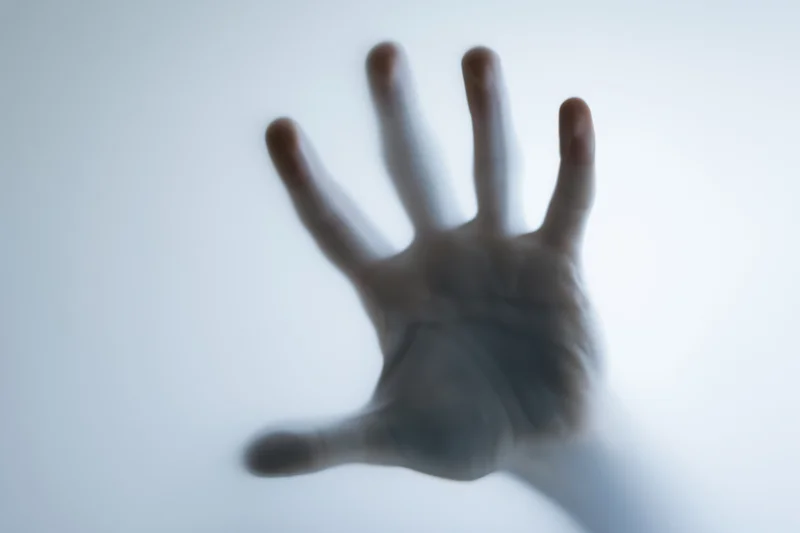 Hand pressing against frosted translucent glass with blurred details and soft light background