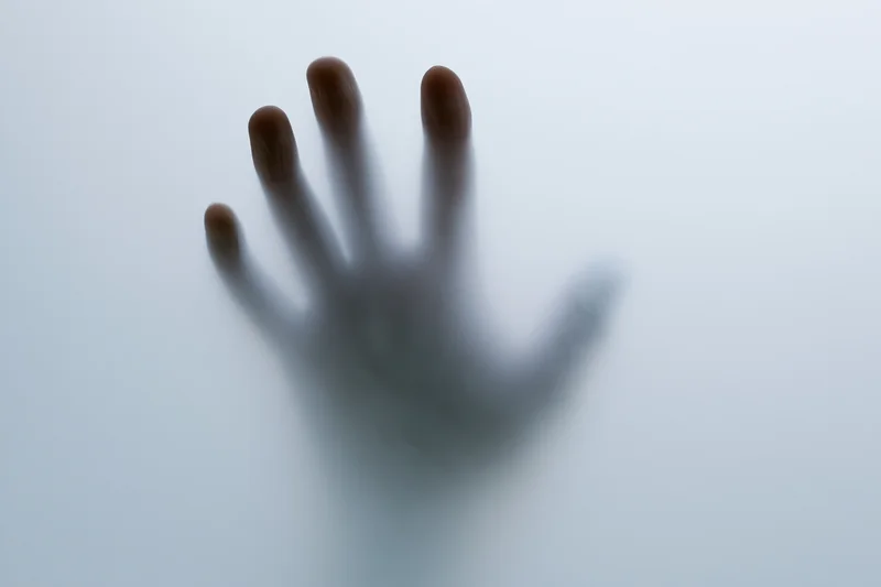Hand pressing against frosted translucent glass, fingers spread, shadow visible through surface