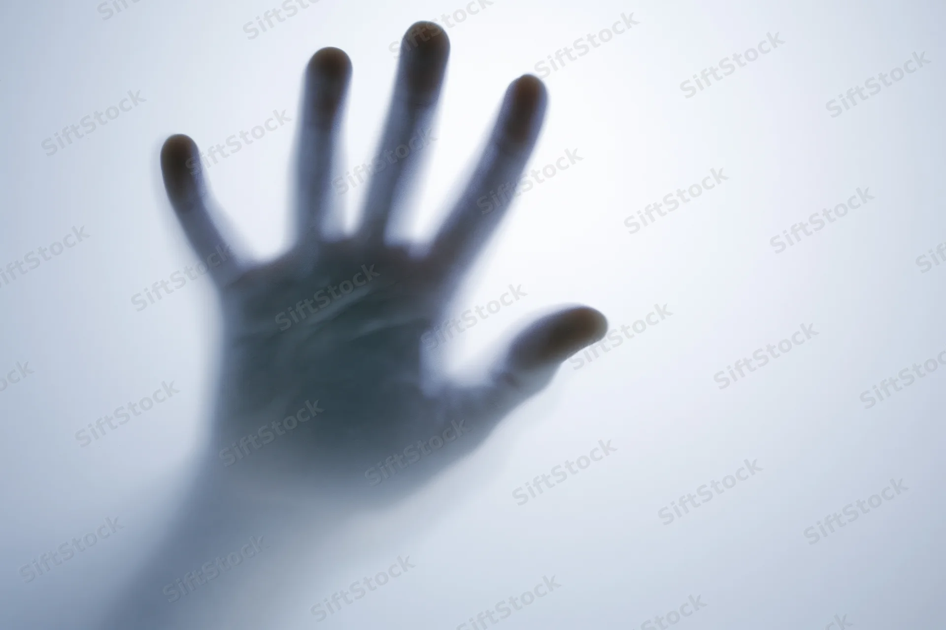 Hand pressing against frosted translucent glass in a blurred silhouette