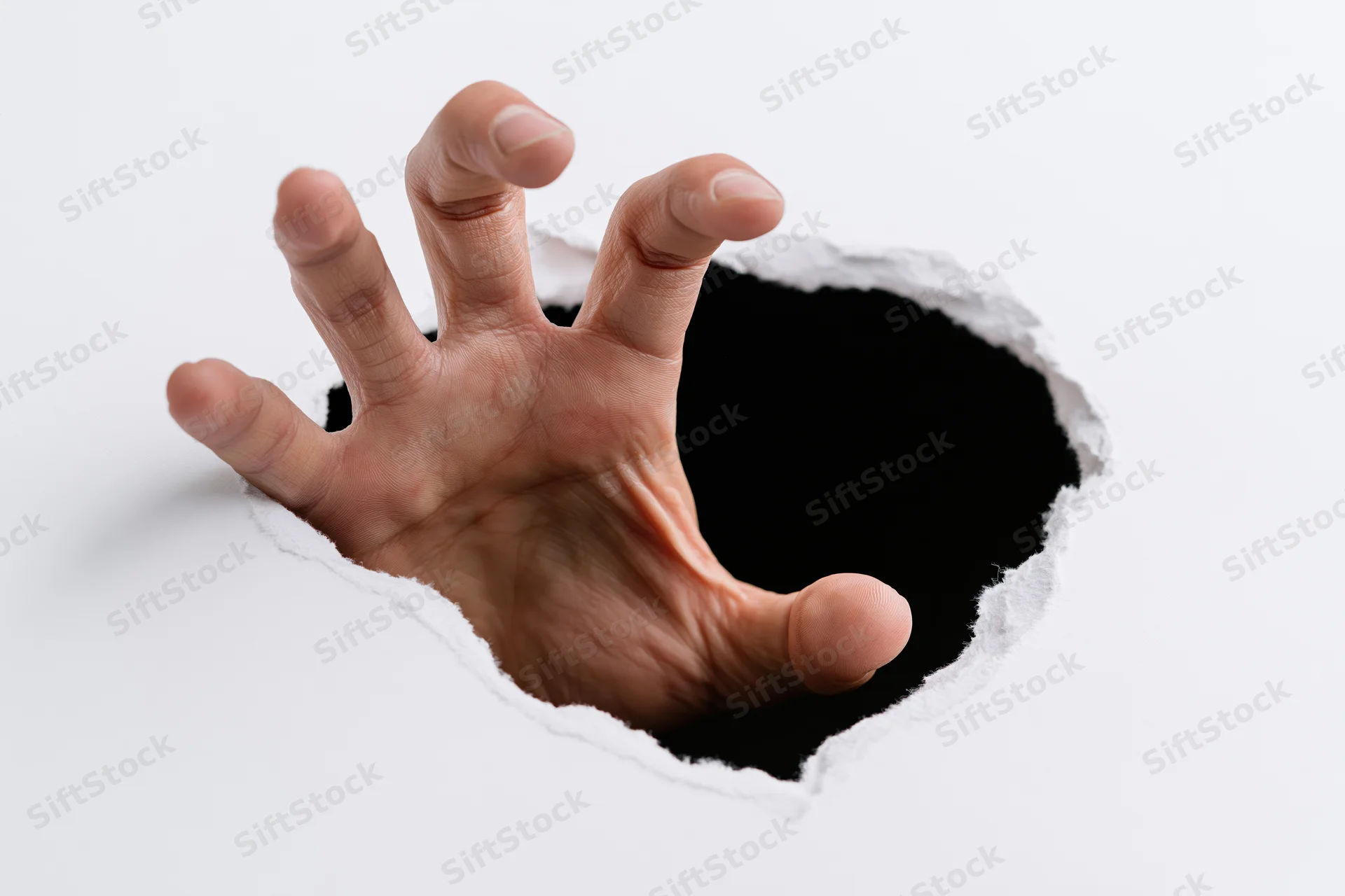 Hand reaching through torn hole in white paper against black background