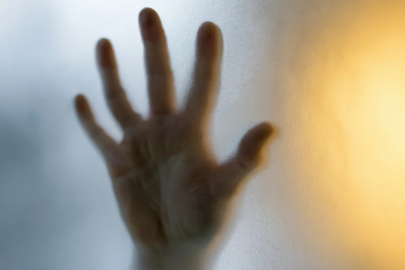 Hand pressed flat against frosted glass with fingers spread in a closeup view