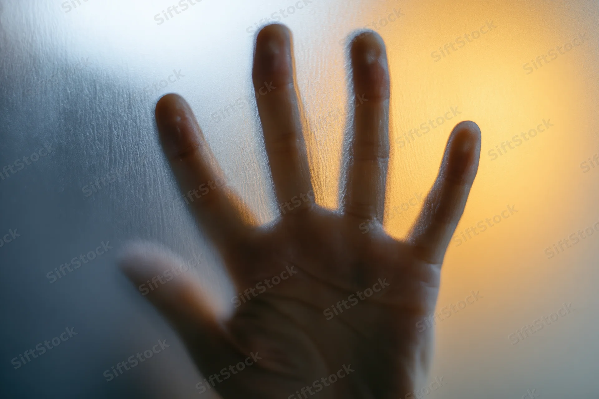 Hand pressed flat against frosted glass with fingers spread, light glowing through from behind
