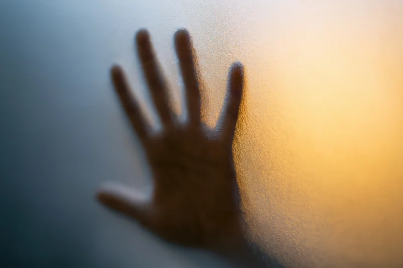 Hand pressed flat against frosted glass with fingers spread, showing silhouette and light gradient