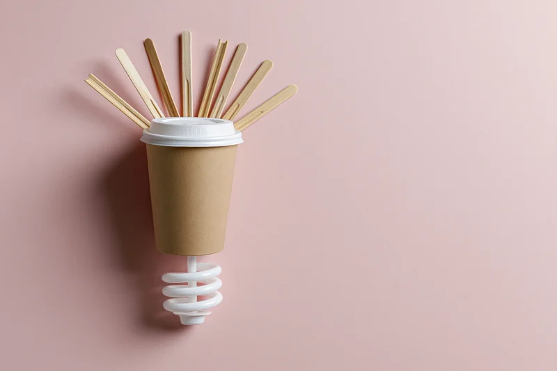 Coffee cup with wooden stirrers arranged as a lightbulb on pink background