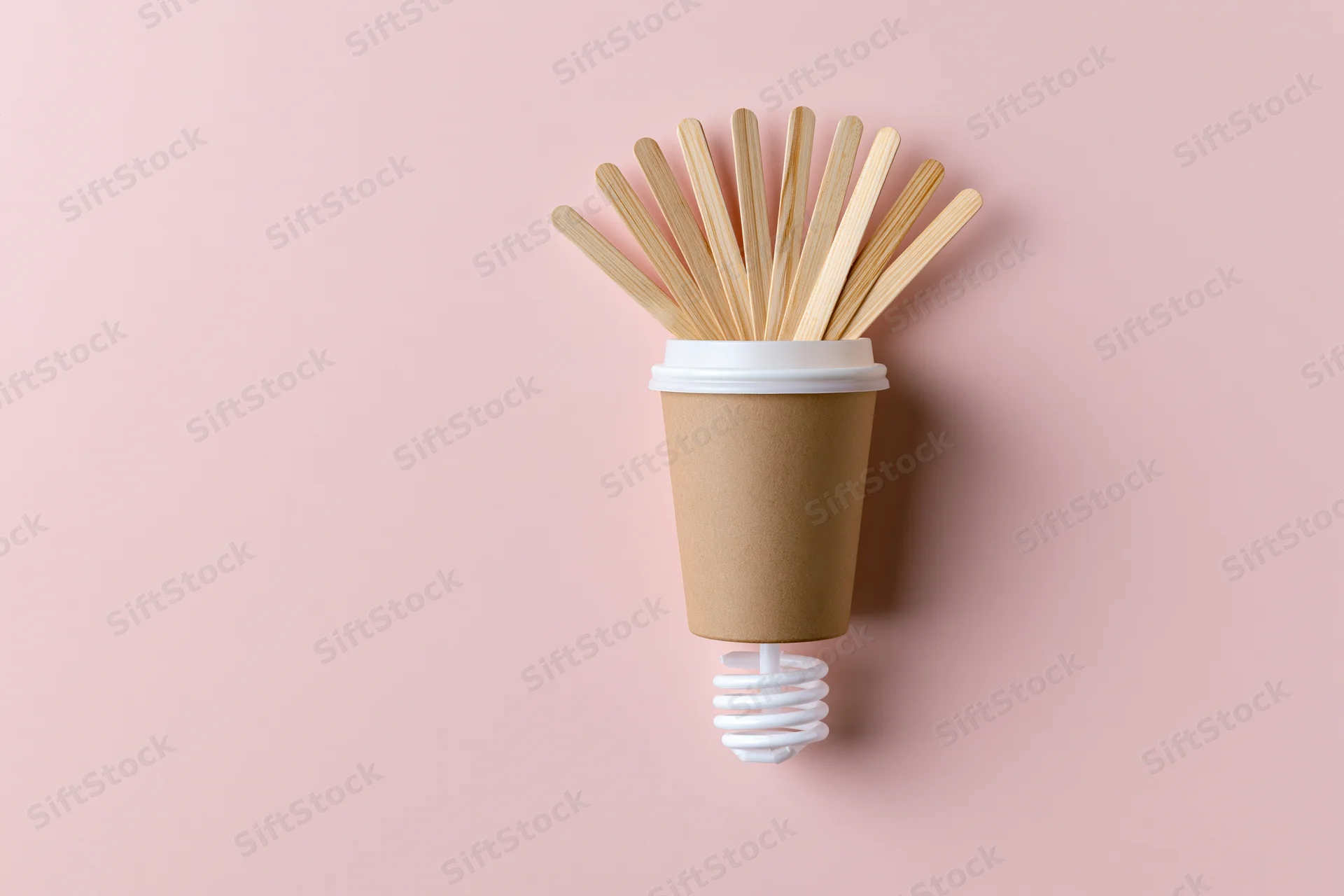 Coffee cup with bamboo stirrers arranged as a lightbulb on a pink background