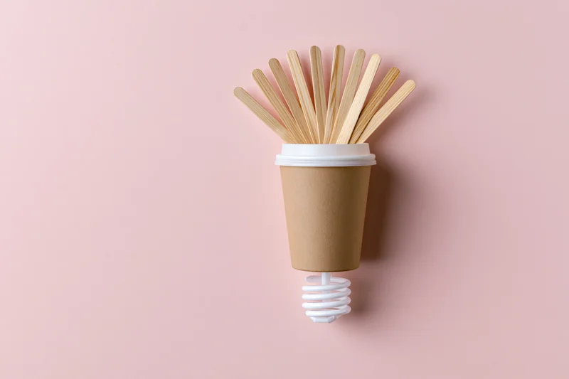 Coffee cup with bamboo stirrers arranged as a lightbulb on a pink background