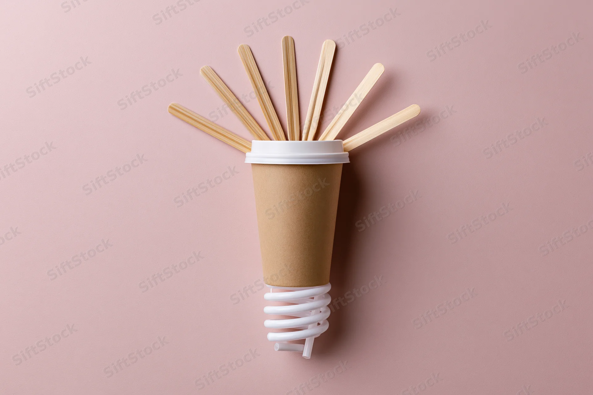 Coffee cup arranged as lightbulb with wooden sticks and spiral base on pink background
