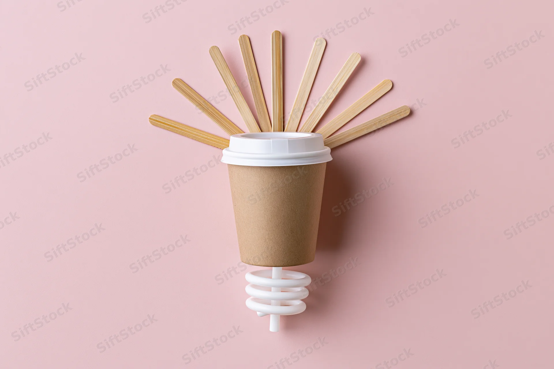 Coffee cup with bamboo sticks arranged as a lightbulb on pink background