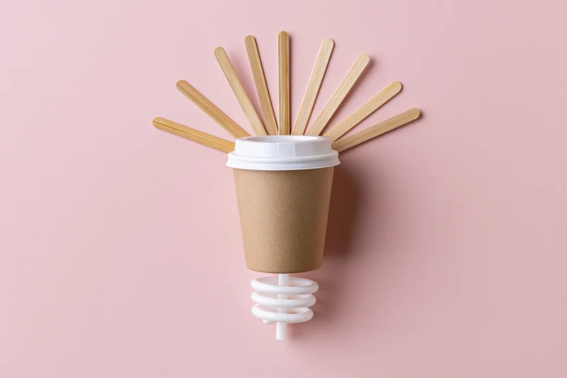 Coffee cup with bamboo sticks arranged as a lightbulb on pink background