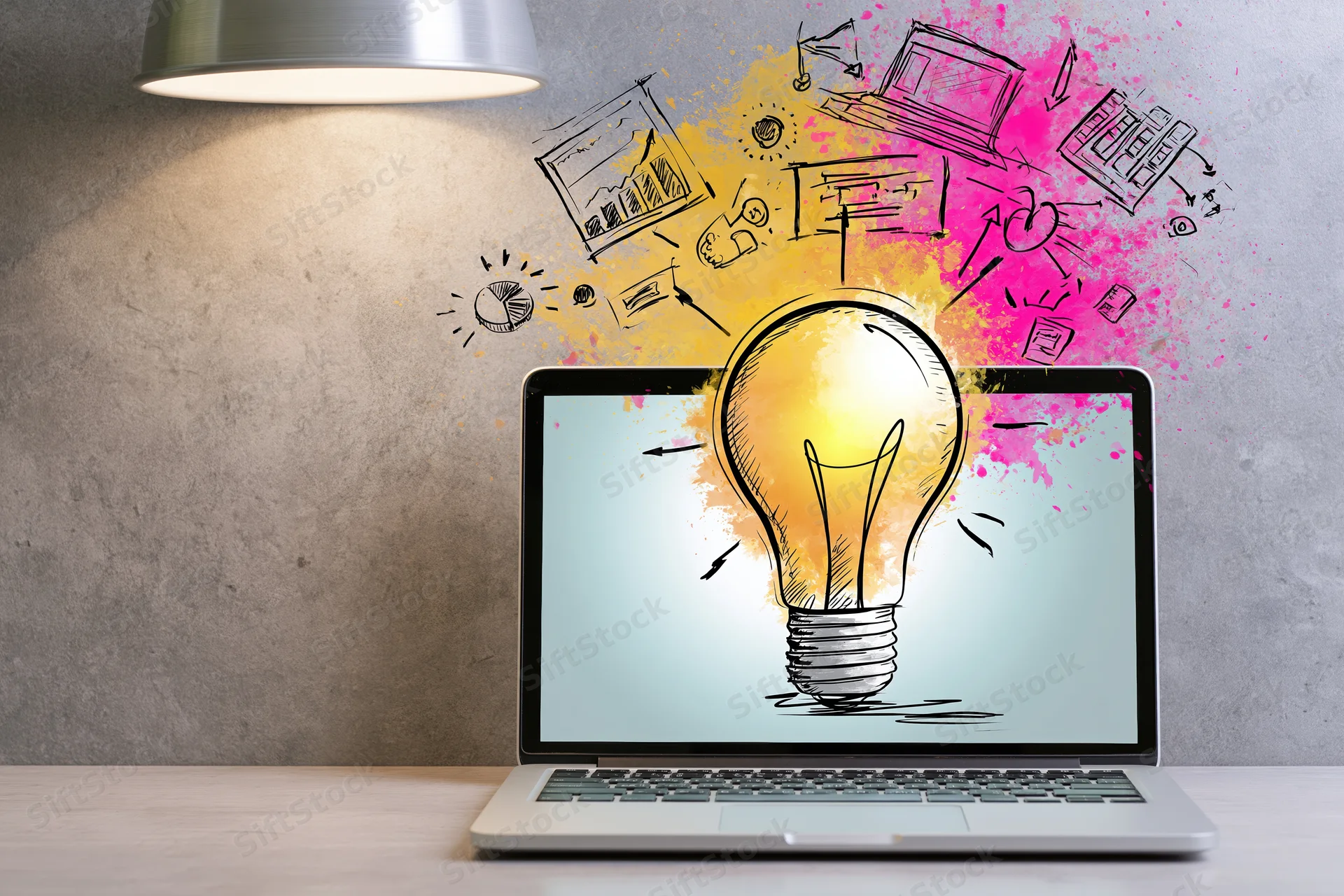 Laptop displaying illustrated lightbulb with surrounding sketches on a desk under a lamp