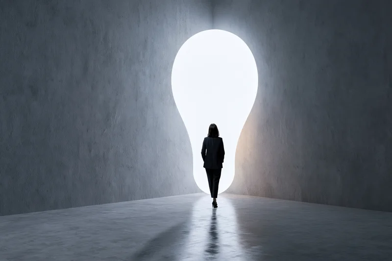 Woman in suit walking toward lightbulb-shaped doorway in concrete interior