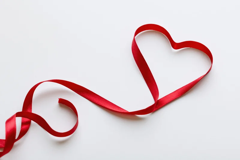 Red satin ribbon shaped into a heart on white background