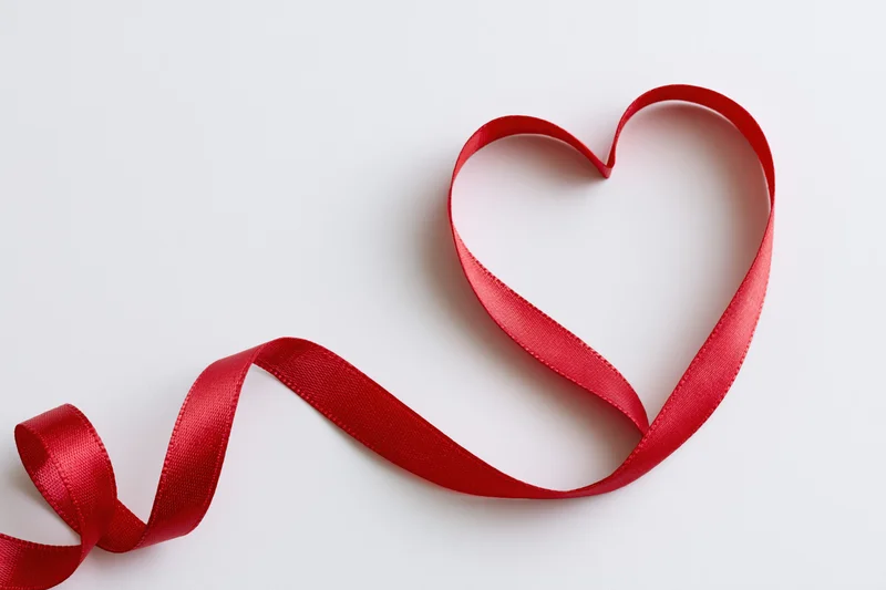 Red satin ribbon shaped into a heart on white surface