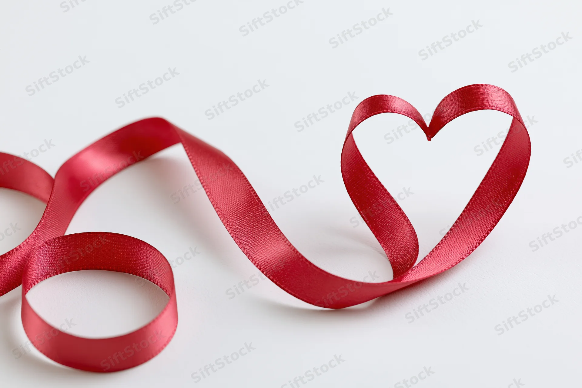 Red satin ribbon shaped into a heart on a white surface