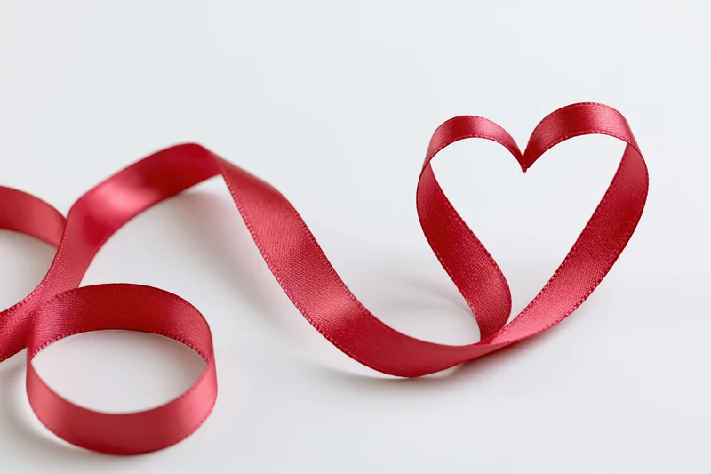 Red satin ribbon shaped into a heart on a white surface