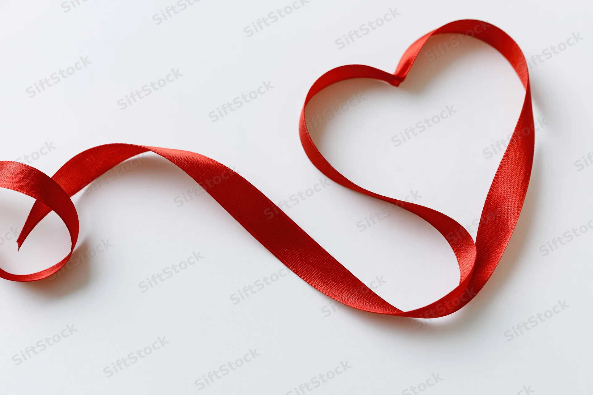 Red satin ribbon shaped into a heart on a white surface