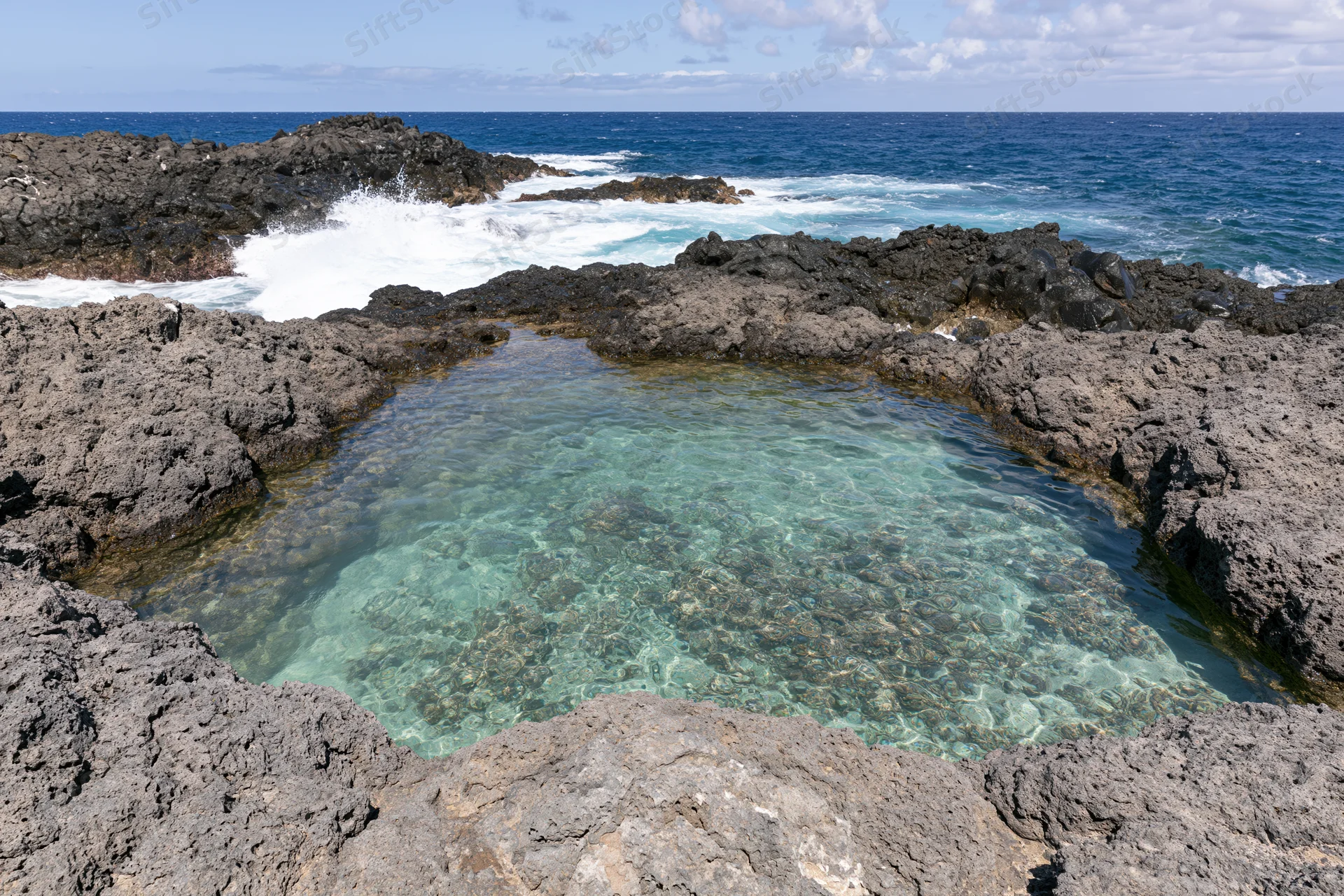 Clear turquoise water in a natural lava rock tidal pool by the ocean