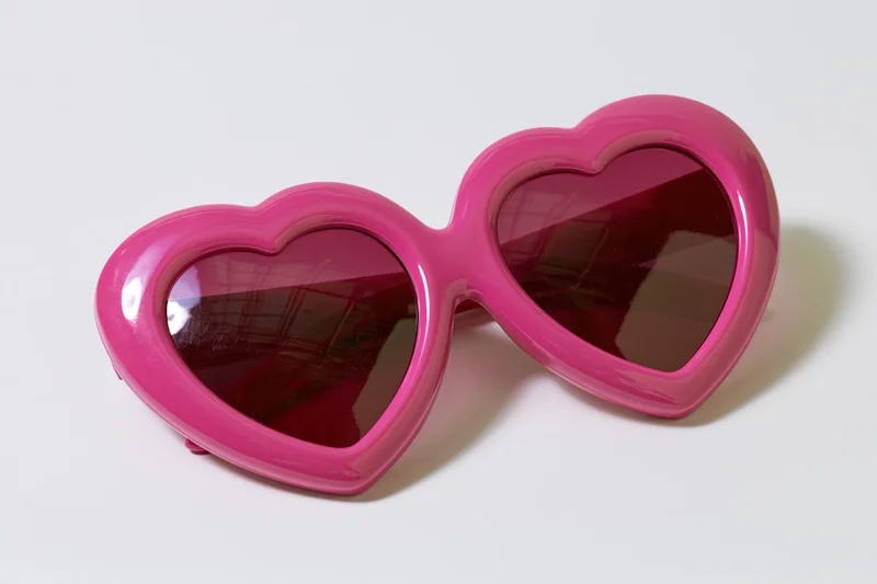 Oversized heart-shaped pink novelty sunglasses lying flat on white surface