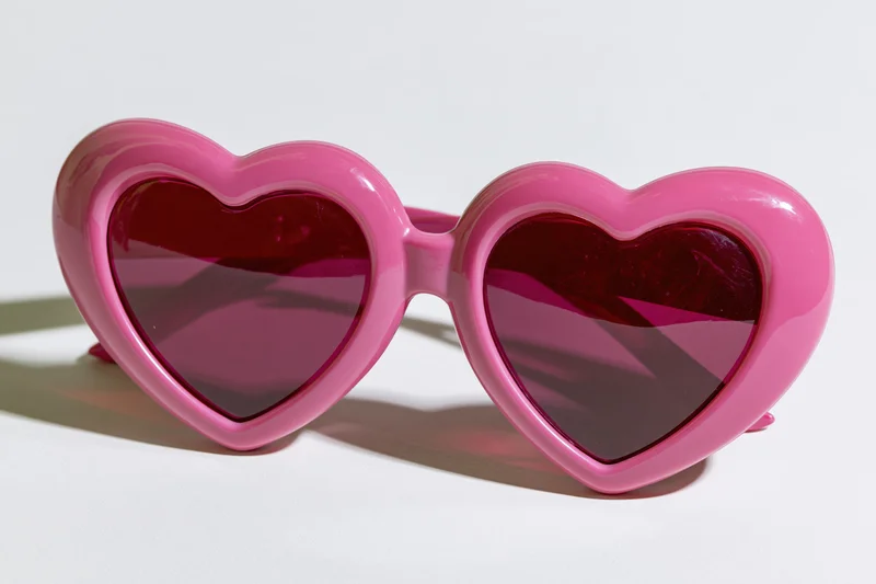Oversized heart-shaped pink novelty sunglasses lying flat on white surface