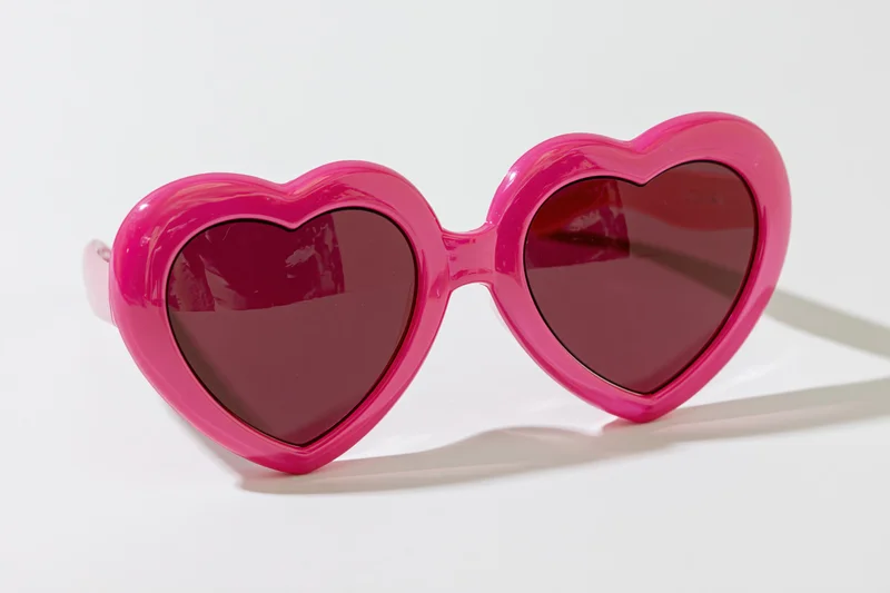 Oversized heart-shaped pink novelty sunglasses lying flat on white surface