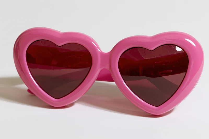 Oversized heart-shaped pink novelty sunglasses lying flat on white surface