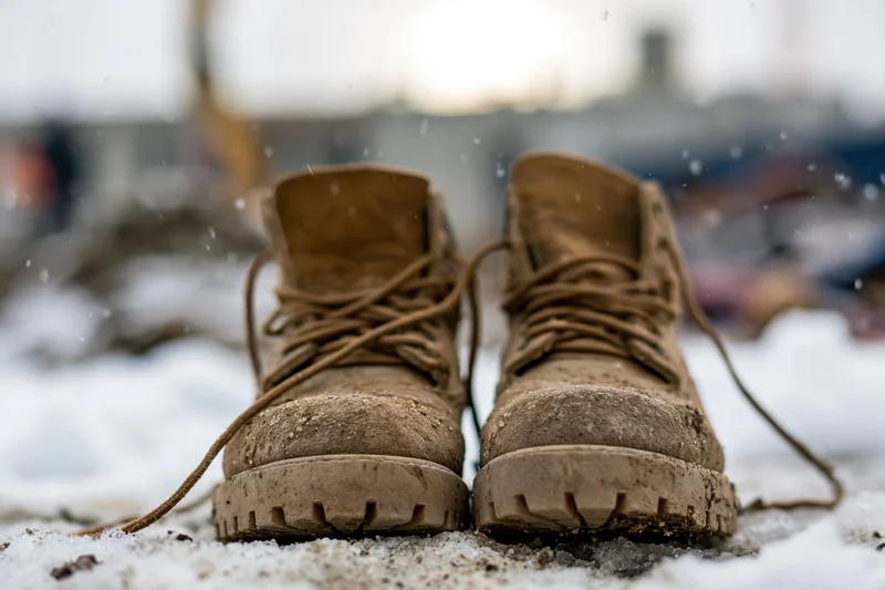 Muddy tan leather work boots resting on snowy ground in winter