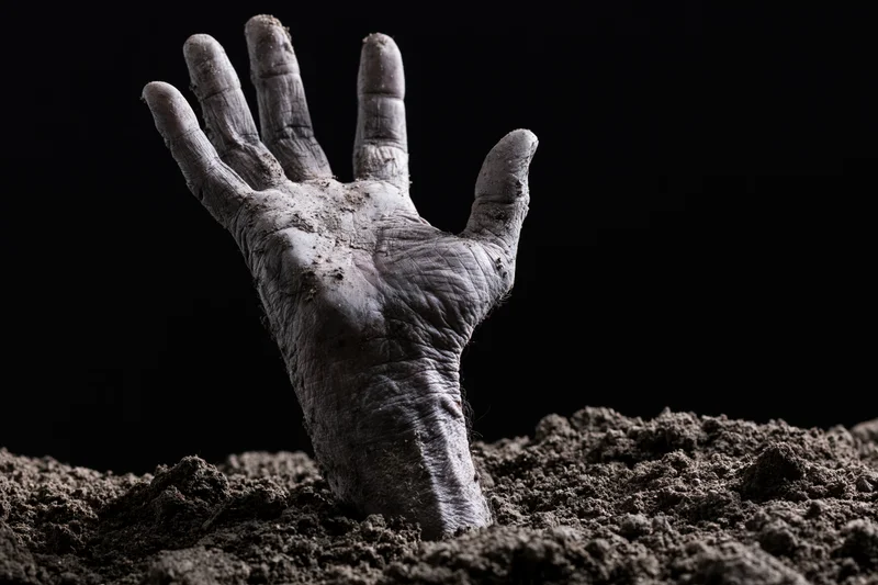 Decayed pale hand reaching upward from dark soil