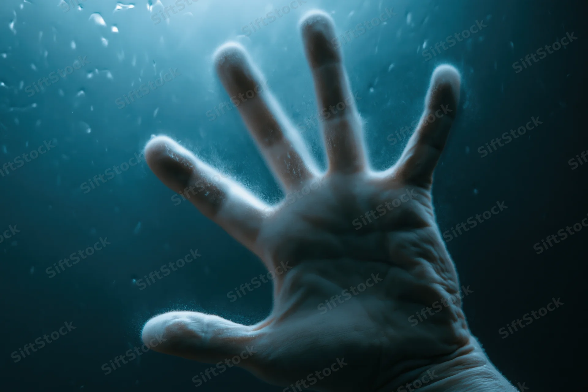 Pale hand pressed against wet glass underwater, fingers spread, light filtering from above