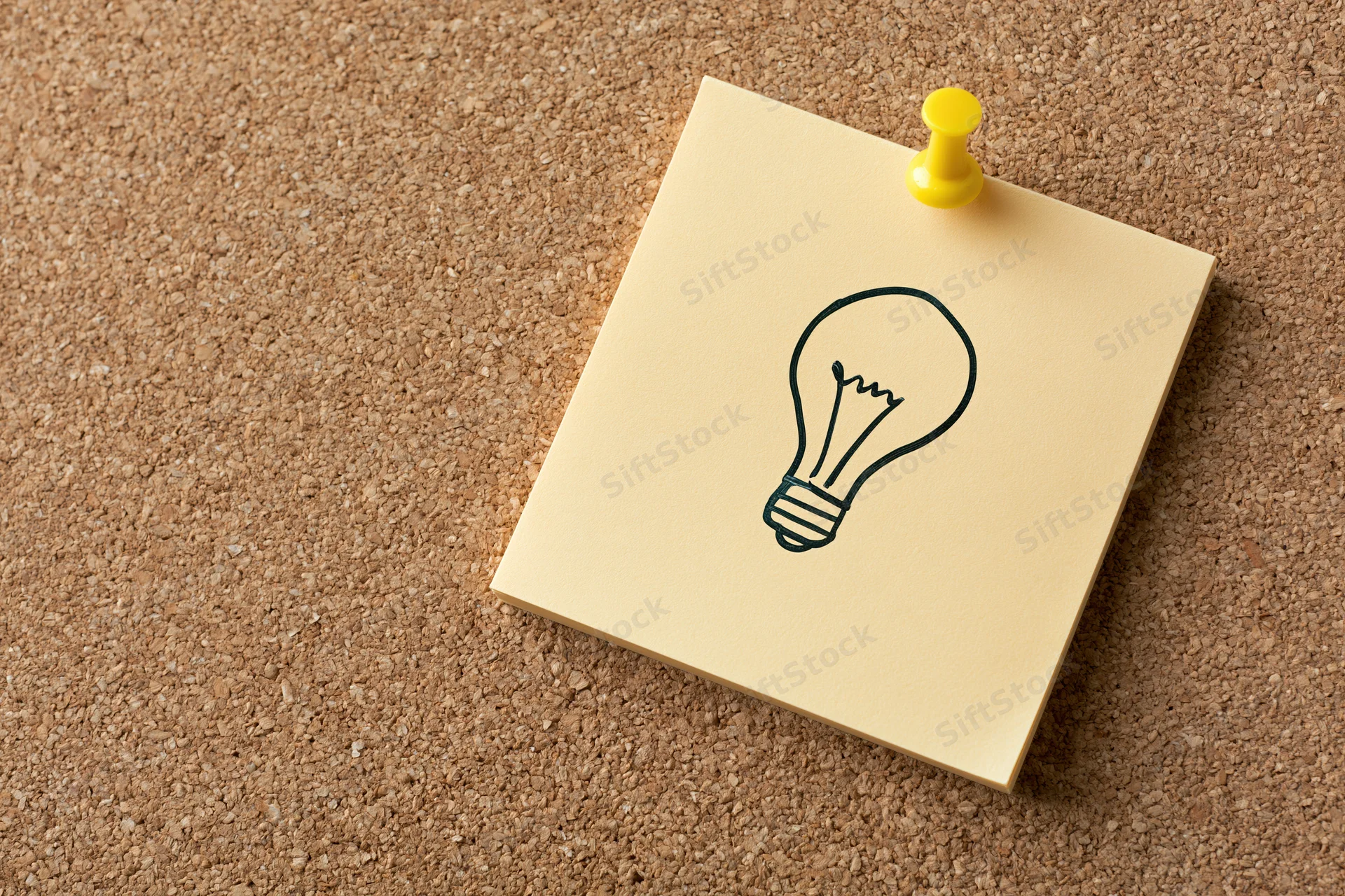 Sticky note with lightbulb drawing pinned to cork board