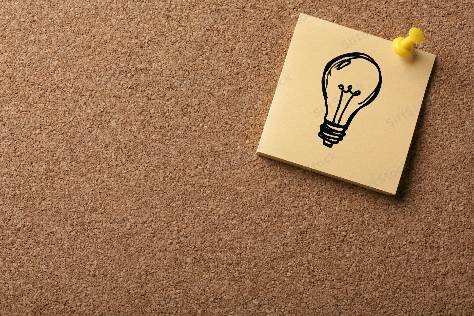 Sticky note with hand-drawn lightbulb pinned to corkboard in office workspace