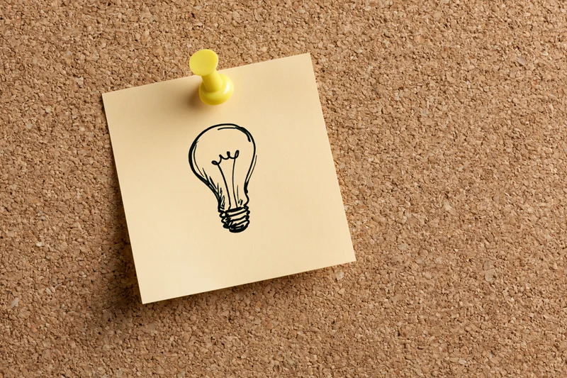 Sticky note with hand-drawn lightbulb pinned to cork board