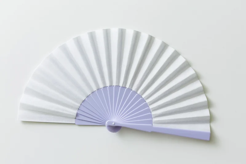 Open folding hand fan with white paper and lavender plastic frame lying flat on white surface