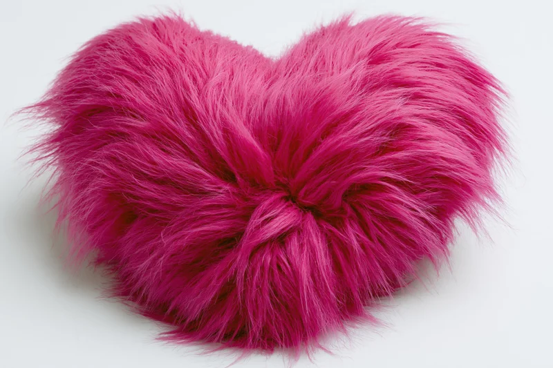 Heart-shaped plush pillow covered in hot pink faux fur on white background