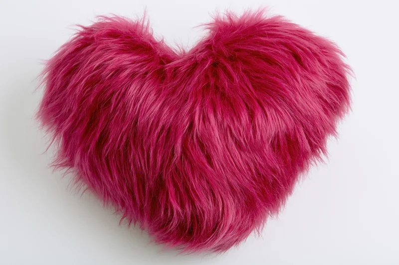 Plush heart-shaped pillow covered in hot pink faux fur on white background