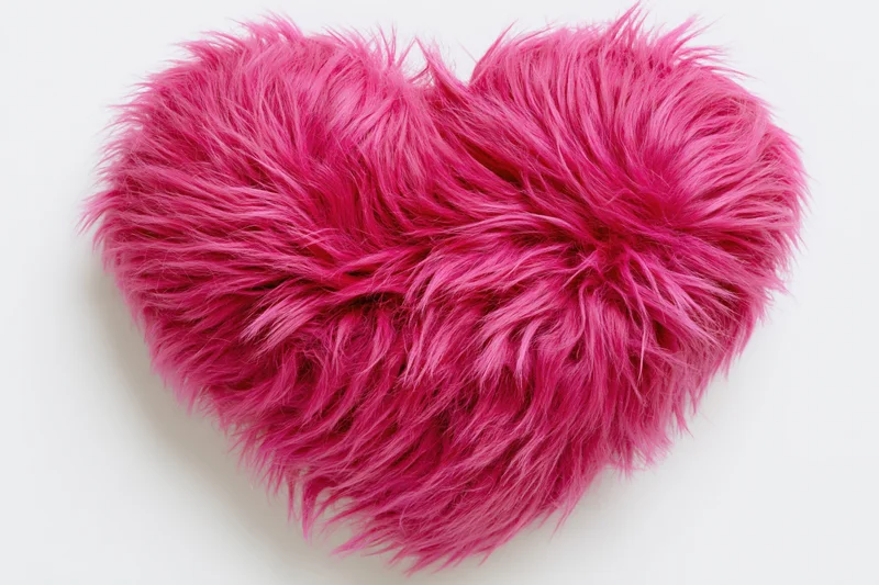 Plush heart-shaped pillow covered in hot pink faux fur on white background