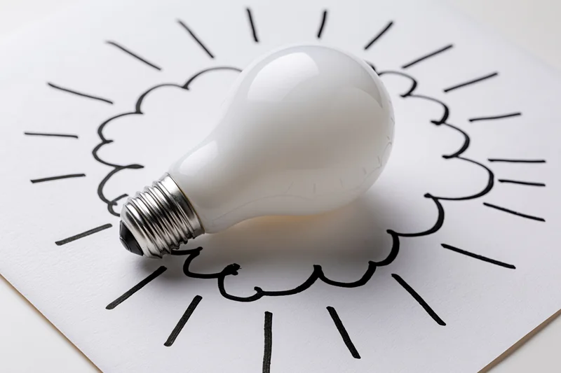 White lightbulb resting on a hand-drawn sun sketch on paper
