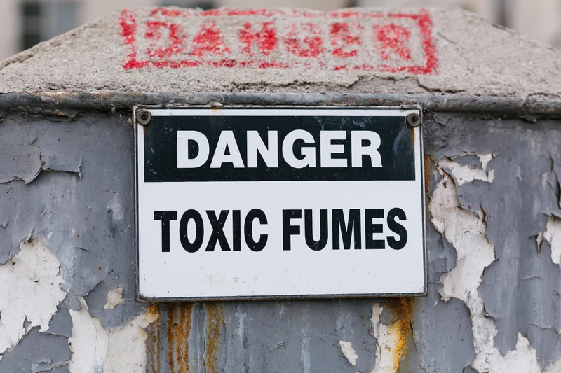 Weathered metal warning sign reading danger toxic fumes mounted on a corroded industrial container