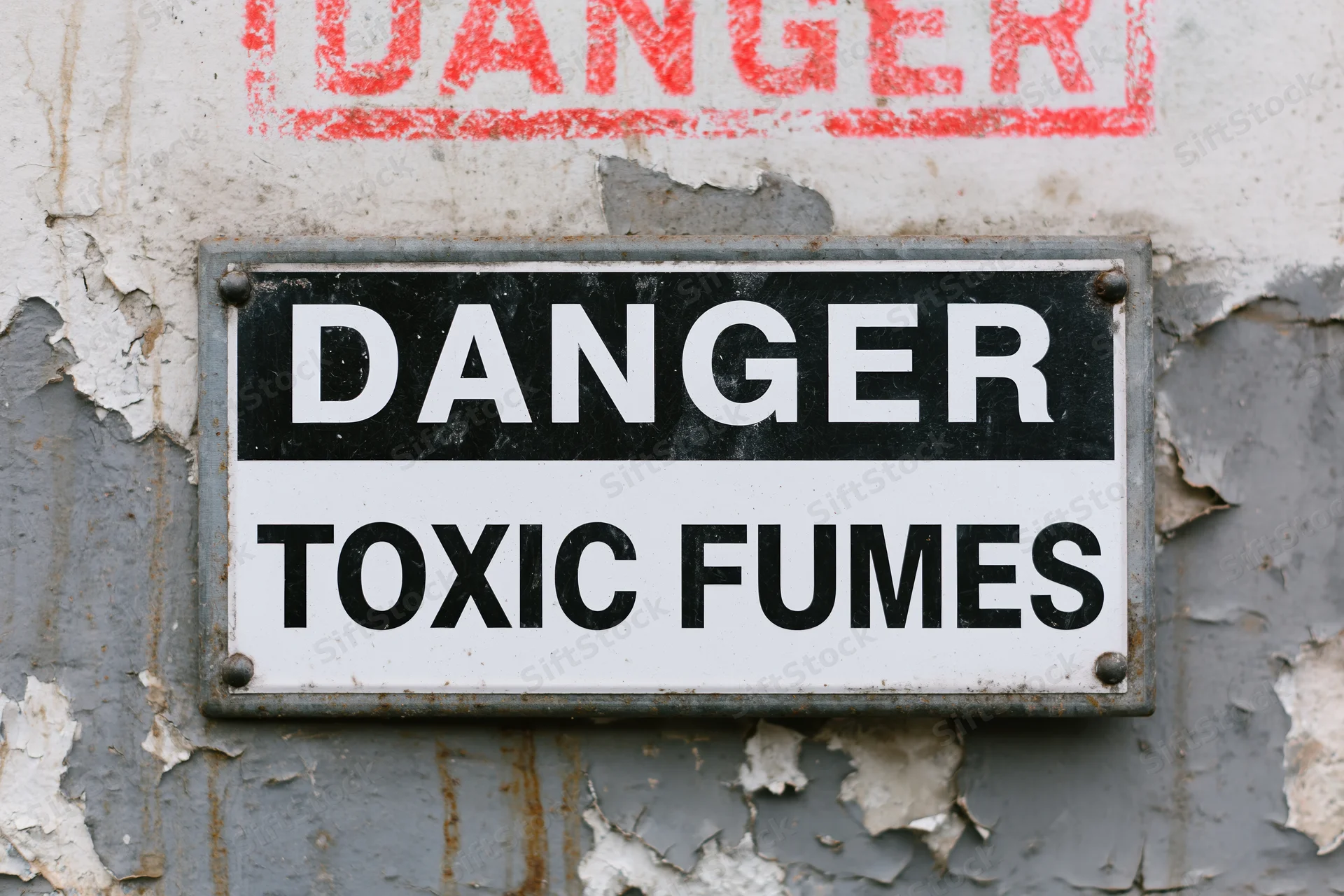 Metal warning sign reading danger toxic fumes mounted on a peeling painted wall