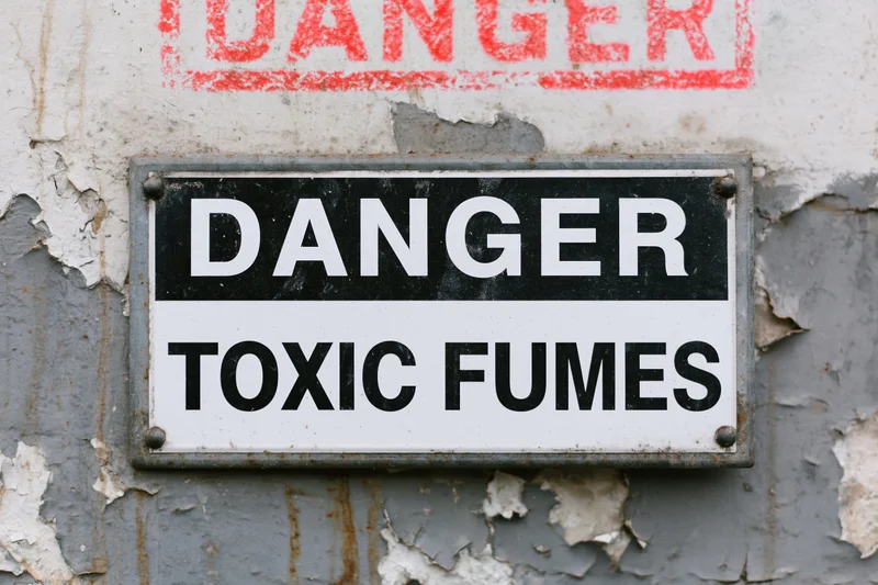 Metal warning sign reading danger toxic fumes mounted on a peeling painted wall