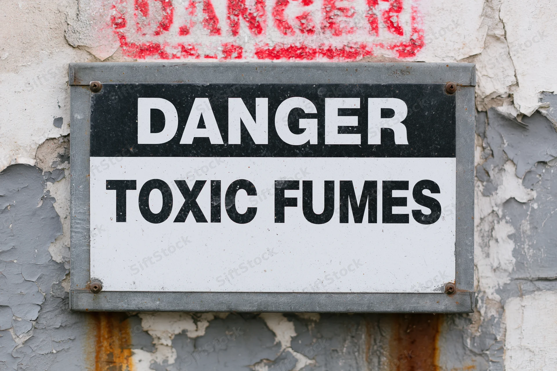 Metal warning sign reading danger toxic fumes mounted on a weathered industrial wall
