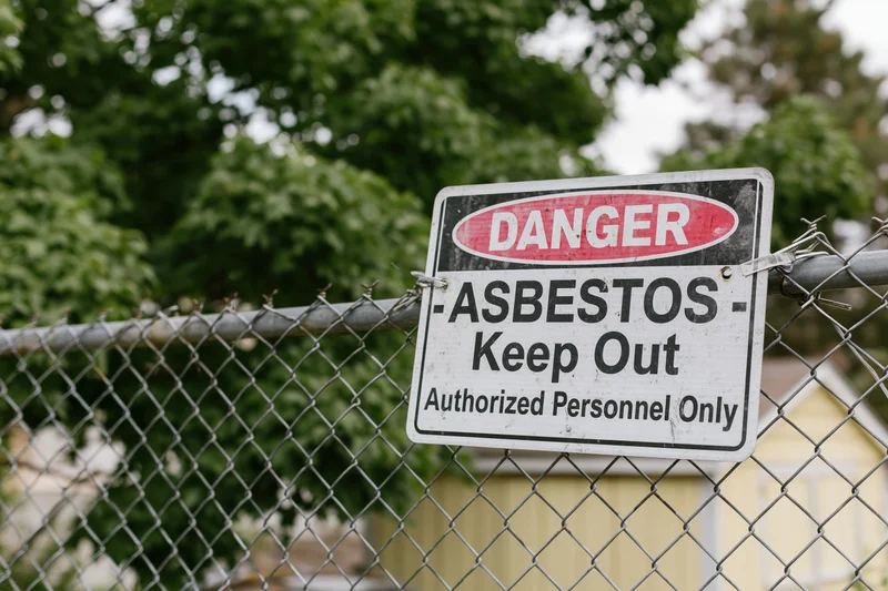 Danger warning sign reading asbestos keep out mounted on chainlink fence outdoors