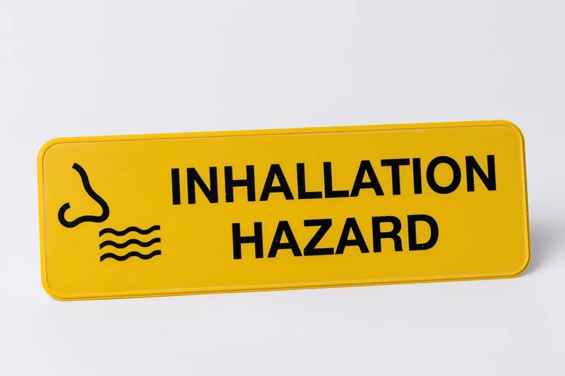 Yellow warning sign reading inhalation hazard with nose and waves symbol on white background