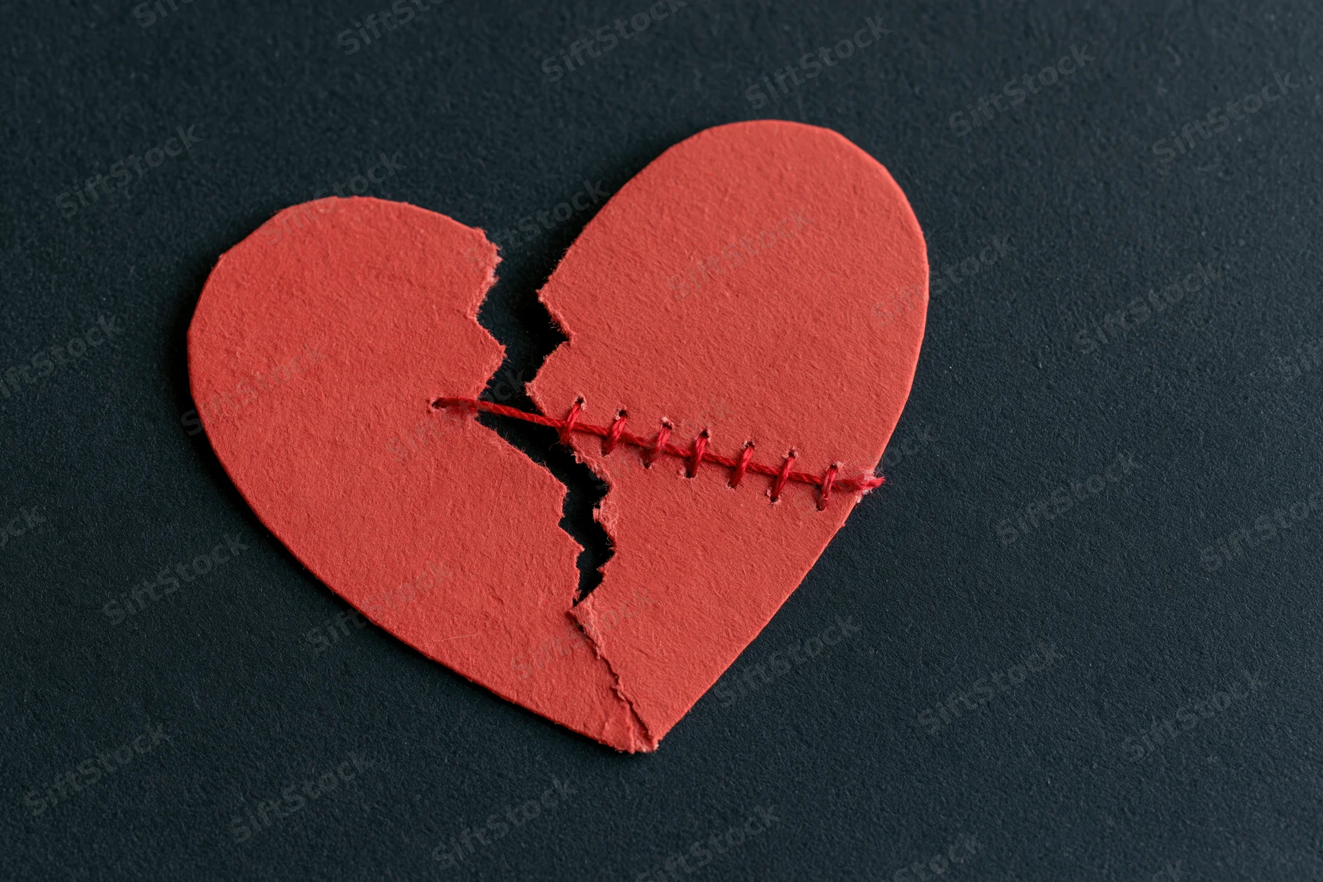 Broken red paper heart stitched back together on black background