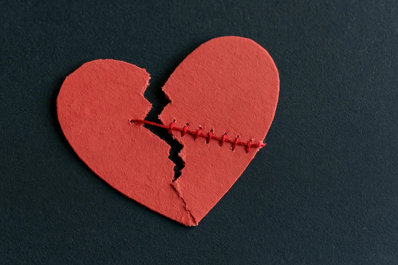 Broken red paper heart stitched back together on black background